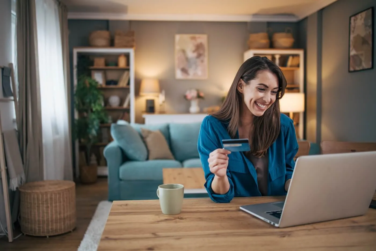Woman smiling while holding a credit card and using a laptop