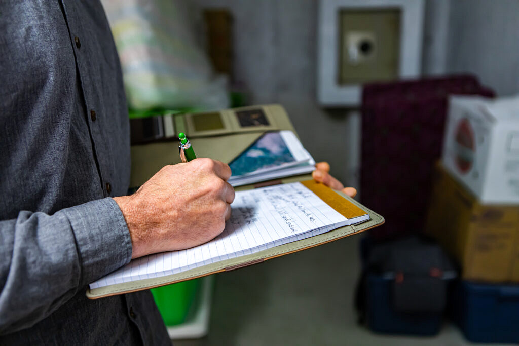 Person in gray shirt writing notes with green pen on a notepad.