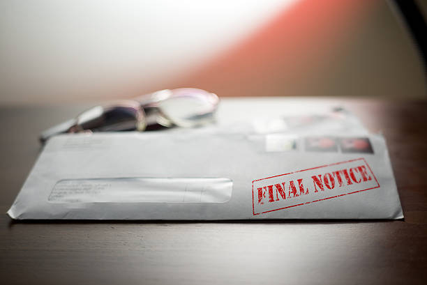 White envelope stamped with red "FINAL NOTICE" text lying on a dark wooden table with reading glasses resting on top.