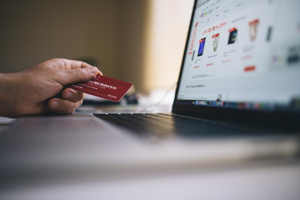 Hand holding red credit card while using a laptop.