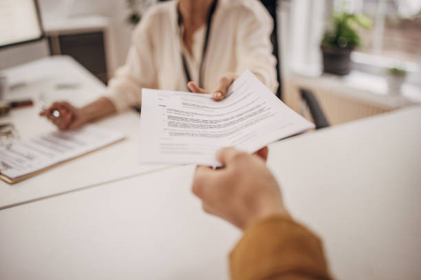 Person handing a document to someone at a desk.