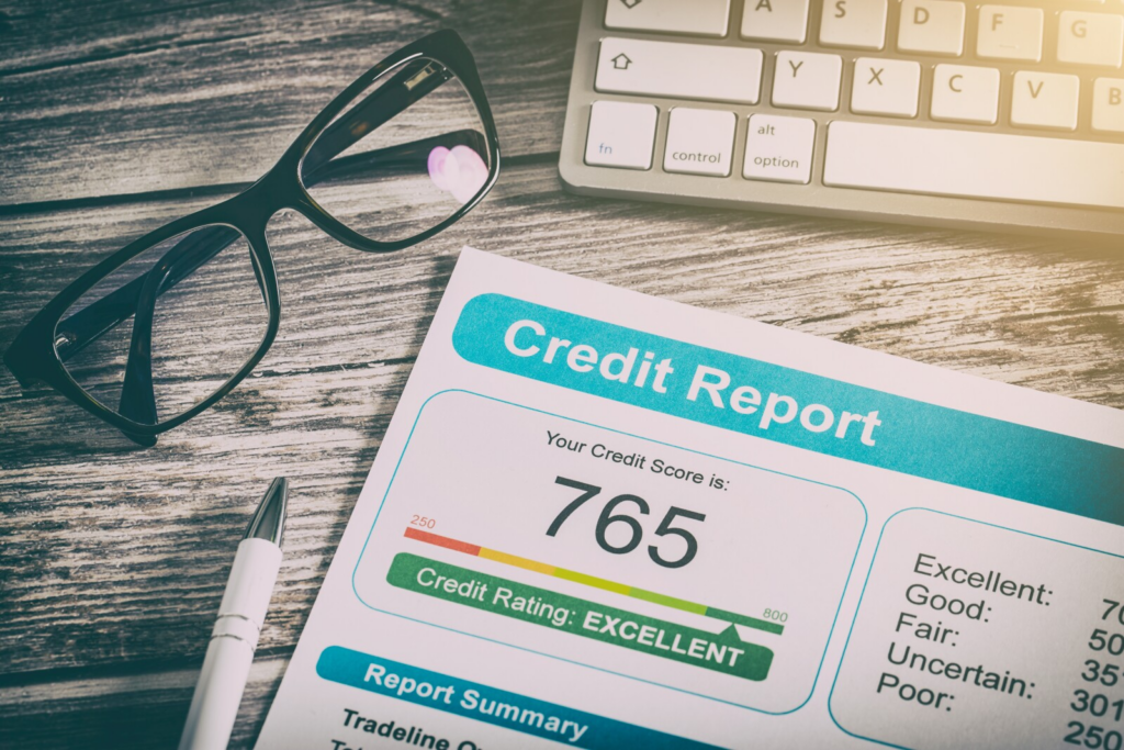 Credit report document showing a score of 765 with "Excellent" rating on a wooden desk with glasses, pen, and keyboard.