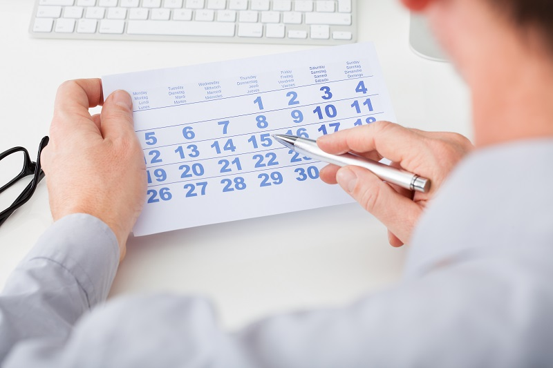 Person holding a calendar and pointing at dates with a pen at a desk.